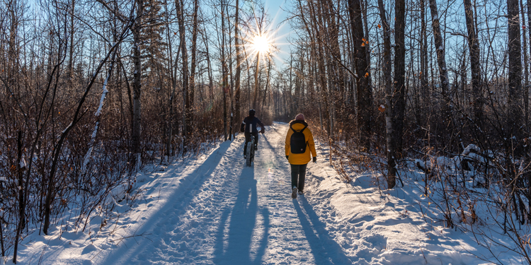 A pedestrian and a cyclist sharing a trail in winter