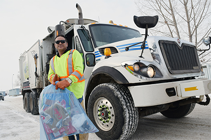 Waste collector holding a blue recycling bag in front of a waste truck