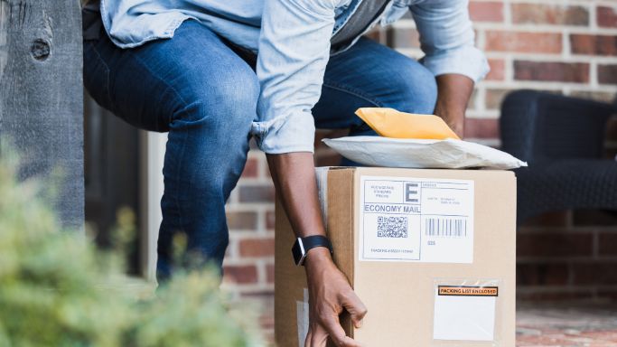 a person picking up a stack of delivered packages at the front door