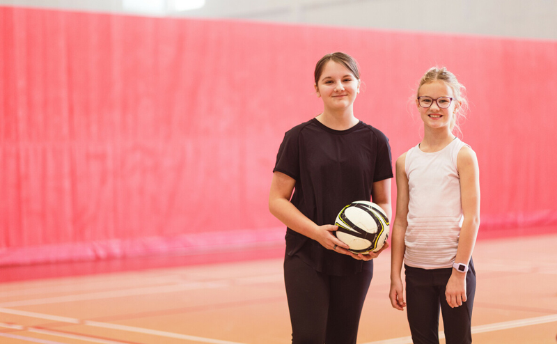 Two kids in a gymnasium. One is holding a ball.