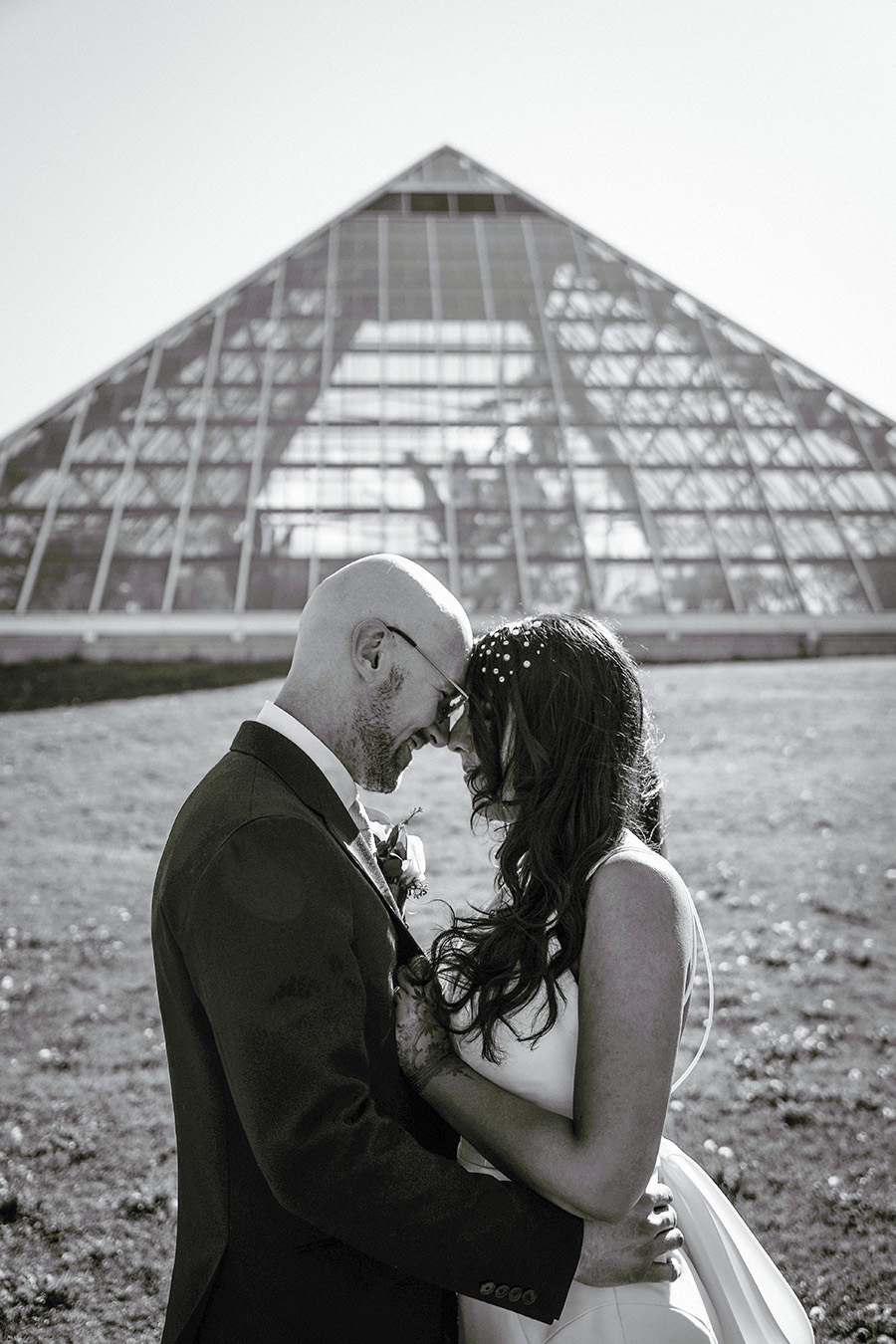 Black & white photo of bride and groom outside and in front of pyramid