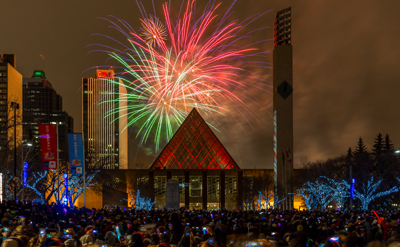 A crowd of people watching fireworks being launched behind City Hall.