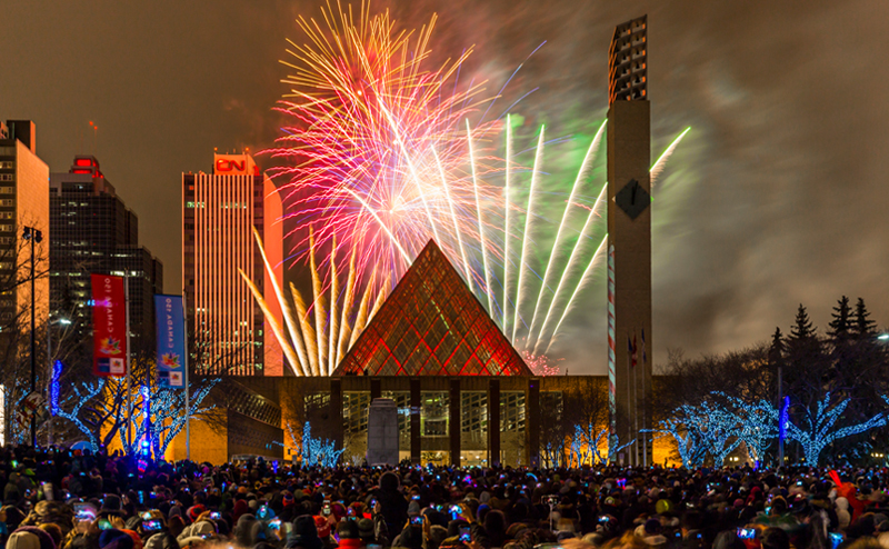 A crowd of people watching fireworks being launched behind City Hall.