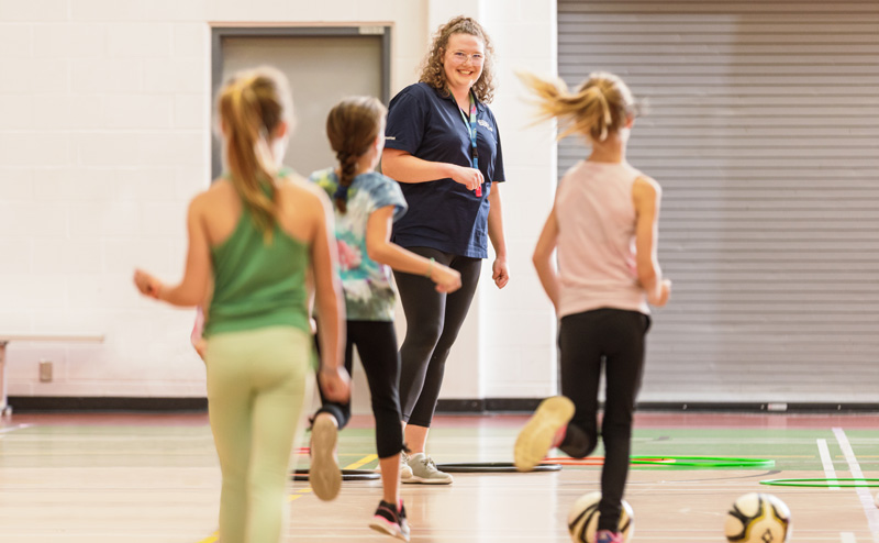 Three girls in a gymnasium, running toward an instructor.