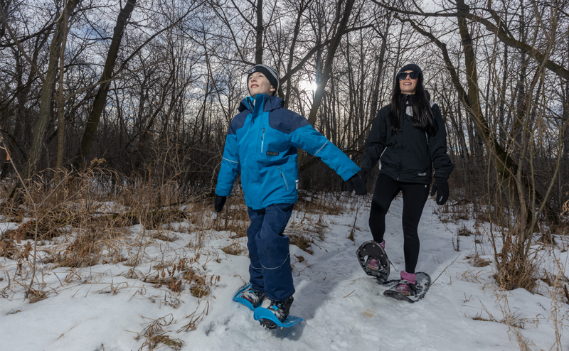 A child and their parent snowshoeing.