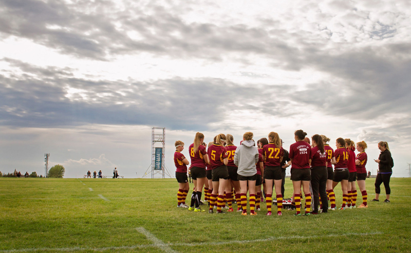 A women's sports team huddled in a field.