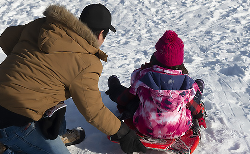 A person guiding their child on a sled at a toboggan hill.