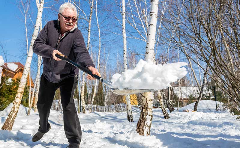 A senior shovelling snow from a sidewalk.