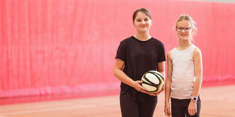 Two kids in a gymnasium. One is holding a ball.