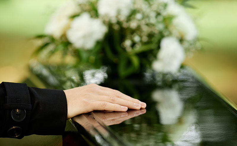 hand on casket with yellow roses